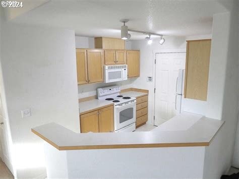 kitchen with white appliances, kitchen peninsula, track lighting, and light brown cabinets