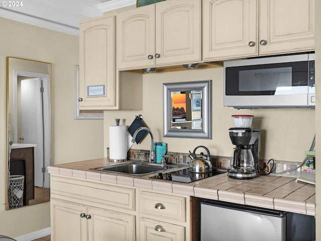 kitchen with tile counters, sink, and cream cabinetry