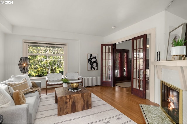 living room with french doors, wood-type flooring, a tile fireplace, and radiator