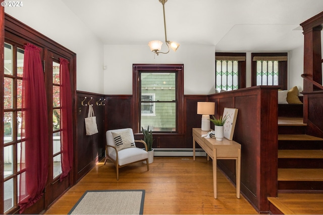 sitting room featuring a notable chandelier, wood walls, wood-type flooring, and a baseboard heating unit