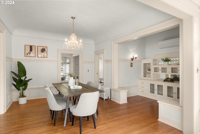 dining room with a wall unit AC, hardwood / wood-style flooring, a chandelier, and radiator