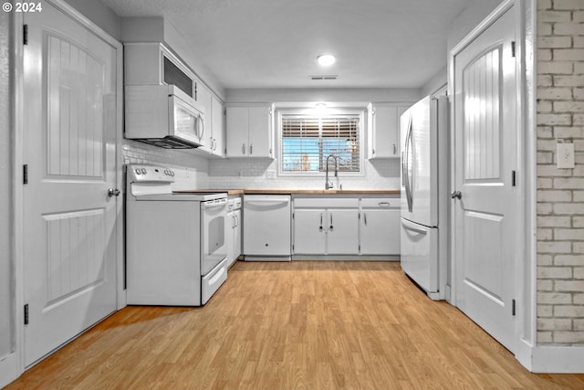 kitchen featuring white cabinetry, sink, light hardwood / wood-style flooring, backsplash, and white appliances