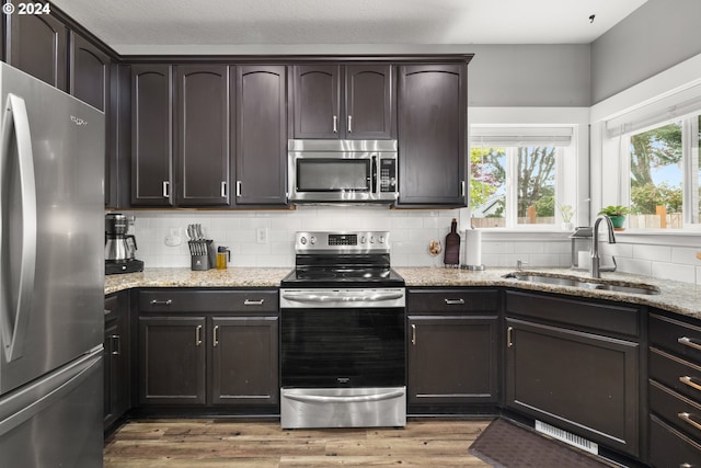 kitchen featuring dark brown cabinets, light stone countertops, sink, and appliances with stainless steel finishes