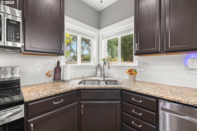 kitchen featuring dark brown cabinetry, stainless steel appliances, light stone counters, and sink