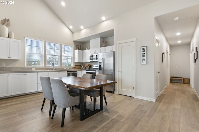 dining area featuring sink, high vaulted ceiling, and light hardwood / wood-style flooring