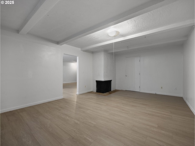 basement featuring light wood-type flooring, a textured ceiling, and a brick fireplace