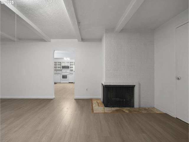 unfurnished living room featuring beam ceiling, hardwood / wood-style flooring, a textured ceiling, and a brick fireplace