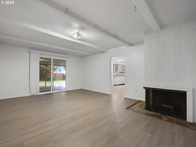 unfurnished living room featuring a textured ceiling, beam ceiling, light wood-type flooring, and a fireplace