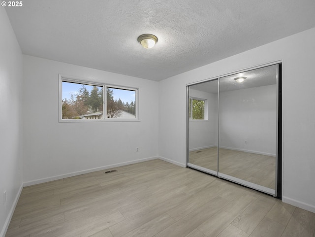 unfurnished bedroom featuring a textured ceiling, light hardwood / wood-style floors, and a closet