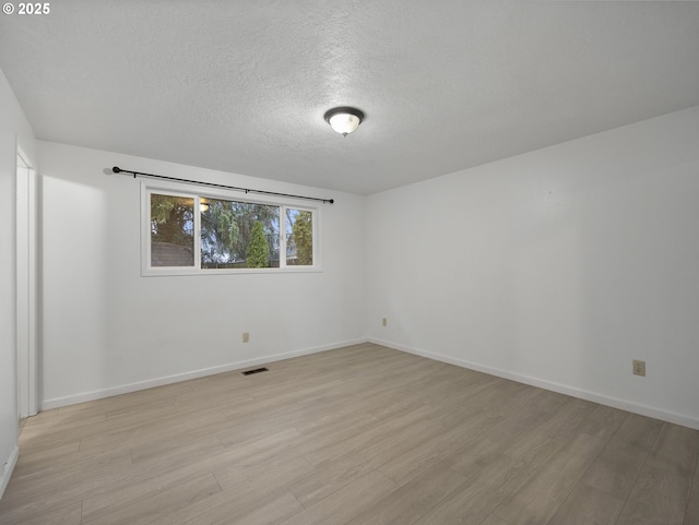 spare room with light wood-type flooring and a textured ceiling