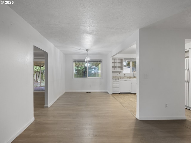 spare room with light hardwood / wood-style floors, a textured ceiling, and an inviting chandelier