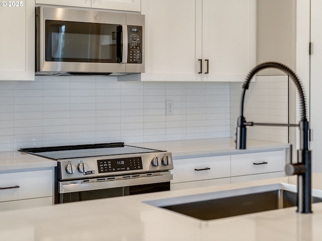 kitchen featuring decorative backsplash, white cabinetry, sink, and appliances with stainless steel finishes