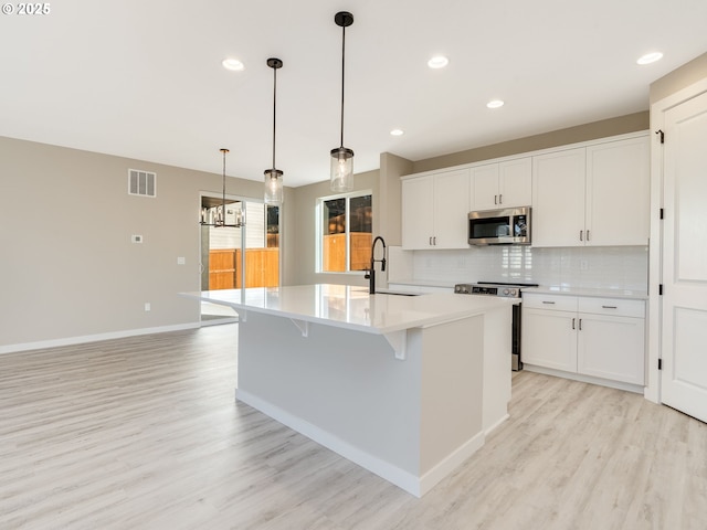 kitchen featuring appliances with stainless steel finishes, sink, white cabinetry, hanging light fixtures, and an island with sink