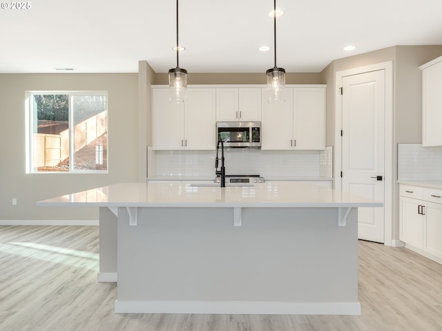 kitchen featuring white cabinetry, a center island with sink, pendant lighting, and light wood-type flooring