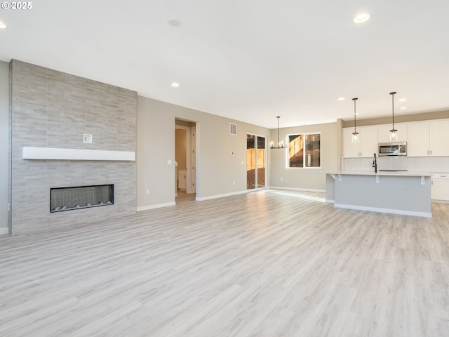 unfurnished living room featuring an inviting chandelier, sink, a tile fireplace, and light hardwood / wood-style flooring