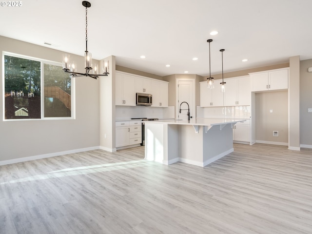 kitchen featuring a kitchen island with sink, light hardwood / wood-style flooring, range with electric stovetop, decorative backsplash, and white cabinets