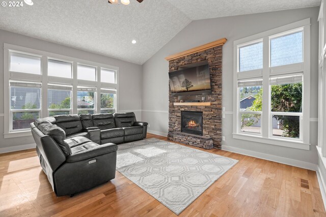 living room with light wood-type flooring, lofted ceiling, a textured ceiling, and a fireplace