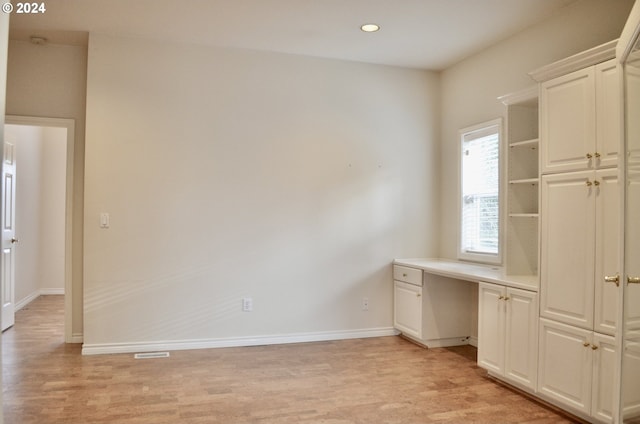 unfurnished office featuring built in desk and light wood-type flooring