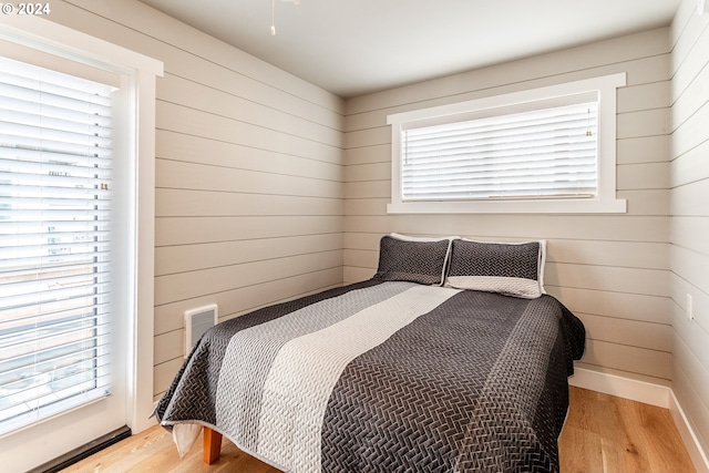 bedroom with access to outside, light hardwood / wood-style floors, and wooden walls