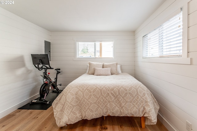 bedroom featuring electric panel, wooden walls, and wood-type flooring