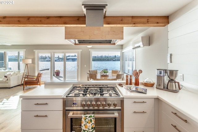 kitchen with white cabinetry, high end stainless steel range oven, a wall mounted AC, light hardwood / wood-style floors, and a water view