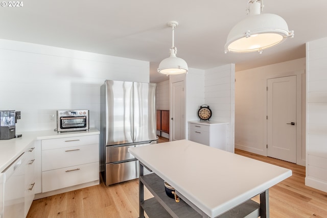 kitchen featuring white cabinets, decorative light fixtures, stainless steel fridge, and light hardwood / wood-style flooring