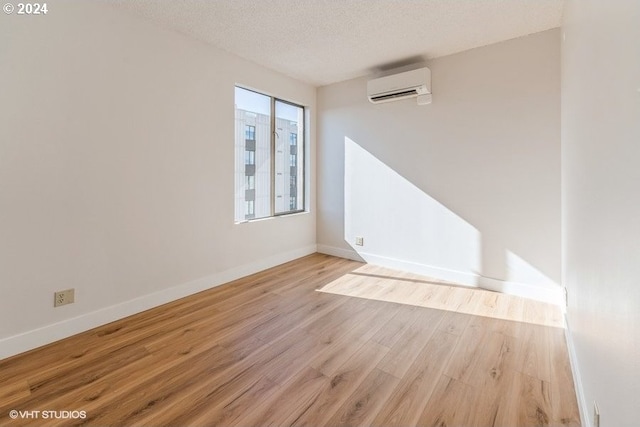 spare room featuring light hardwood / wood-style flooring, a wall mounted air conditioner, and a textured ceiling