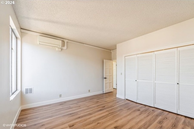 unfurnished bedroom featuring a closet, a wall unit AC, light wood-type flooring, and a textured ceiling