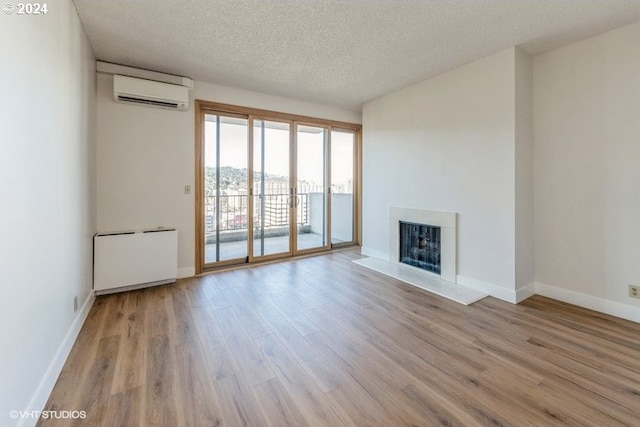 unfurnished living room with light hardwood / wood-style flooring, a wall mounted AC, a textured ceiling, and radiator heating unit