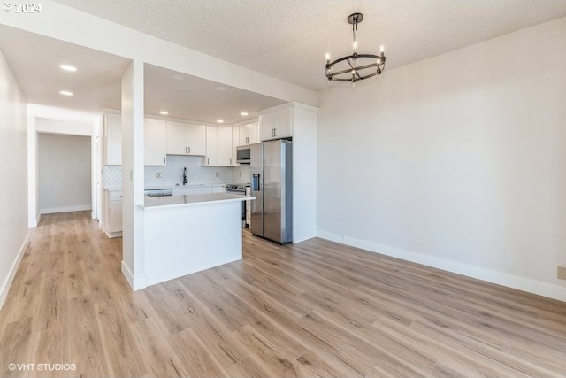 kitchen with appliances with stainless steel finishes, white cabinets, a notable chandelier, light hardwood / wood-style floors, and decorative light fixtures