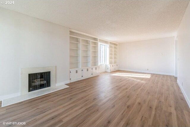 unfurnished living room with built in shelves, light hardwood / wood-style flooring, and a textured ceiling