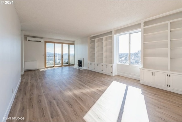 spare room with a textured ceiling, a wall unit AC, light hardwood / wood-style floors, and built in shelves