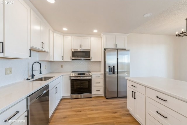 kitchen featuring appliances with stainless steel finishes, sink, light wood-type flooring, white cabinetry, and a chandelier