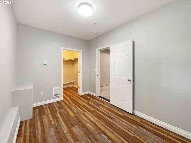 unfurnished bedroom featuring a walk in closet, a closet, and dark hardwood / wood-style floors