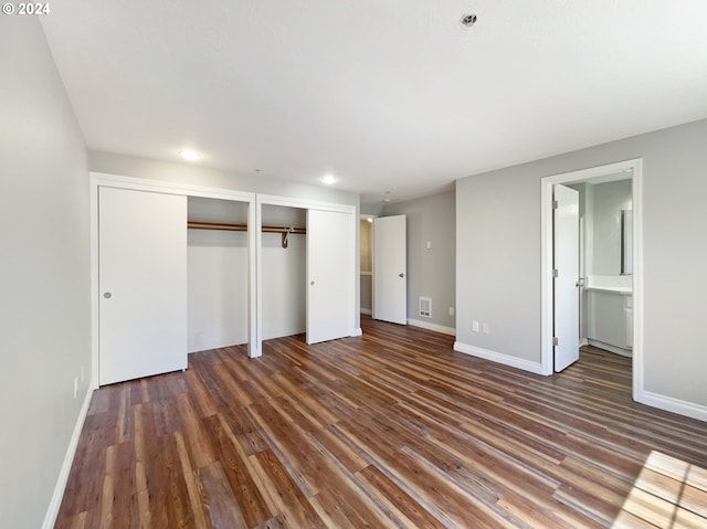 unfurnished bedroom featuring two closets, dark wood-type flooring, and ensuite bathroom