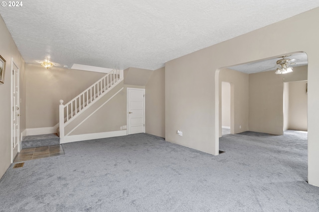 unfurnished living room with light carpet, ceiling fan, and a textured ceiling