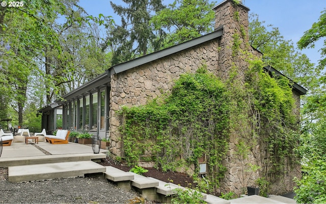 view of property exterior featuring a wooden deck, an outdoor hangout area, stone siding, and a chimney