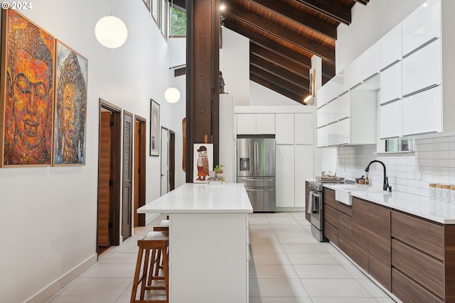 kitchen featuring a center island, high vaulted ceiling, sink, appliances with stainless steel finishes, and a kitchen bar