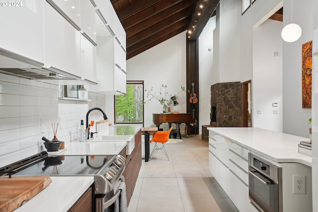 kitchen with high vaulted ceiling, a sink, decorative backsplash, modern cabinets, and stainless steel appliances