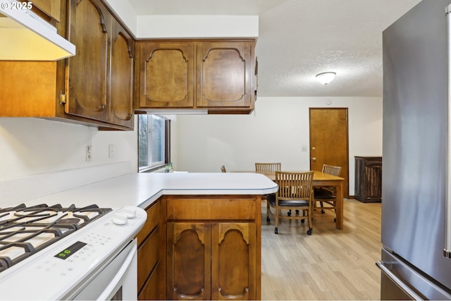 kitchen with stainless steel fridge, light hardwood / wood-style floors, a textured ceiling, white range with gas cooktop, and kitchen peninsula