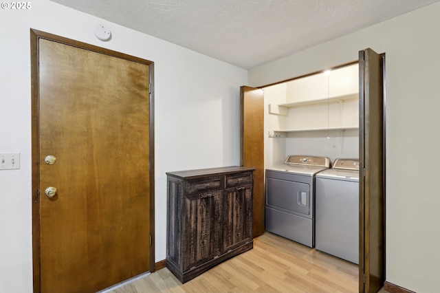 washroom with washing machine and clothes dryer, light hardwood / wood-style flooring, and a textured ceiling