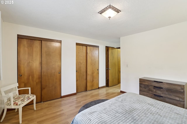 bedroom featuring a textured ceiling, light hardwood / wood-style flooring, and two closets