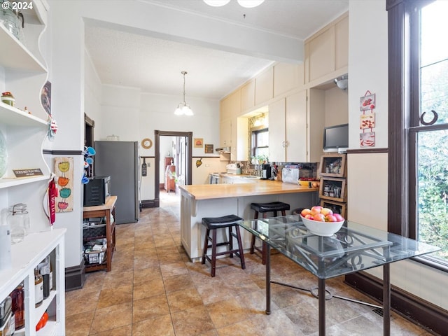 kitchen with hanging light fixtures, a breakfast bar, wood counters, cream cabinetry, and stainless steel fridge