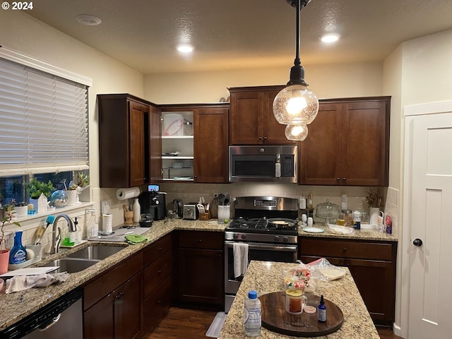 kitchen with appliances with stainless steel finishes, light stone counters, pendant lighting, dark hardwood / wood-style floors, and sink