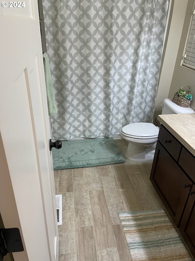 bathroom with wood-type flooring, vanity, walk in shower, and toilet