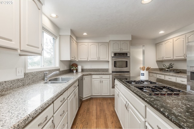 kitchen with black gas cooktop, recessed lighting, light wood-style flooring, double oven, and a sink