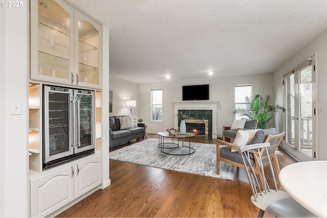 living area with wine cooler, a fireplace, a textured ceiling, and wood finished floors