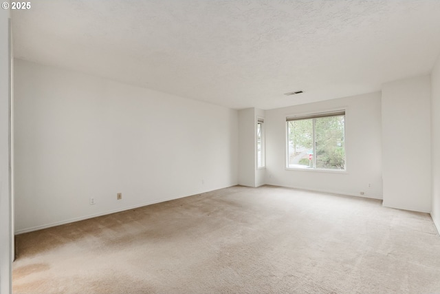 spare room featuring visible vents, light colored carpet, a textured ceiling, and baseboards