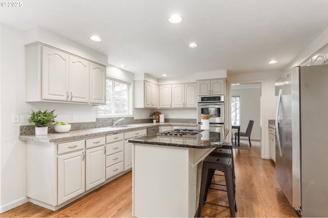 kitchen with light wood finished floors, a breakfast bar area, a center island, stainless steel appliances, and a sink