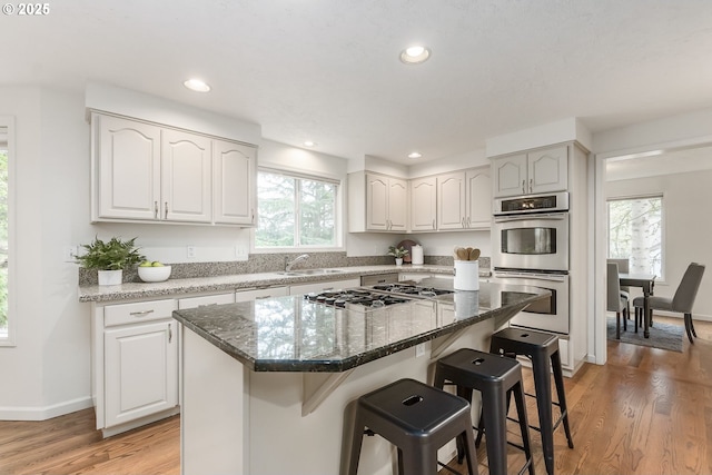 kitchen featuring light wood-style flooring, recessed lighting, a breakfast bar, appliances with stainless steel finishes, and dark stone counters